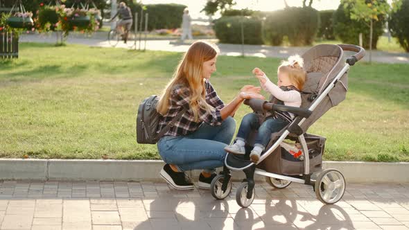 A Young Mother with Her Daughter in a Baby Carriage Communicates