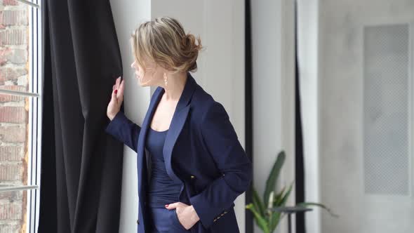 A Blonde Woman in a Blue Suit Poses Looks Out the Window in a Photo Studio