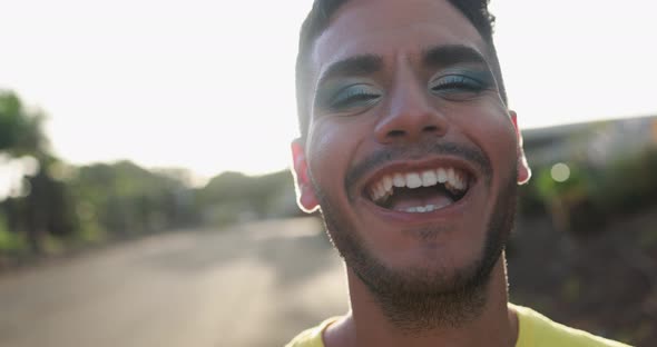 Young happy transgender man with makeup smiling on camera with sunset in the background