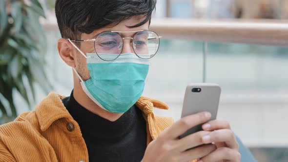 Closeup Young Arab Guy in Protective Mask Typing Message on Smartphone Using Mobile Application