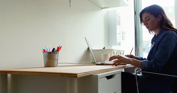 Female executive talking on mobile phone while using laptop