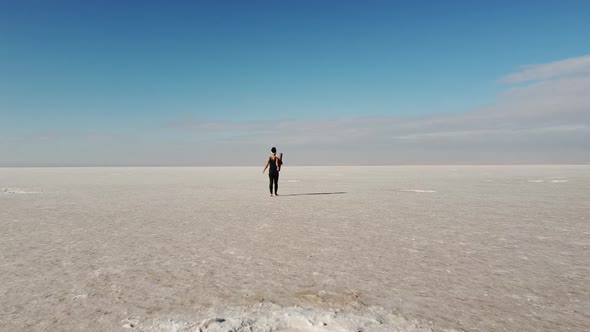 Beautiful young woman walking with a yoga mat in the middle of a salt flat. She is unrolling the mat
