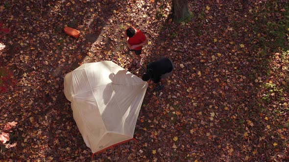 A drone shot of two-men assembling a camping tent in an autumn forest in West Virginia.