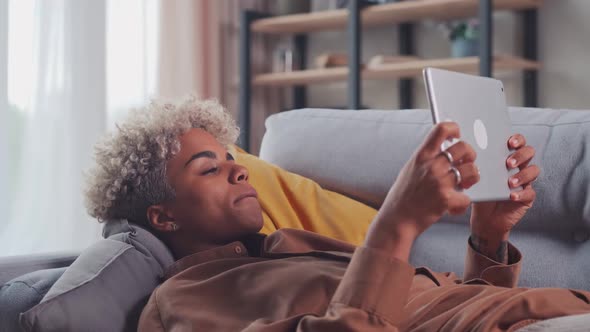 African Woman Lying on Sofa Studying Design Apps on Digital Computer Tablet