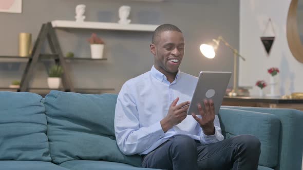 African Man Making Video Call on Tablet on Sofa