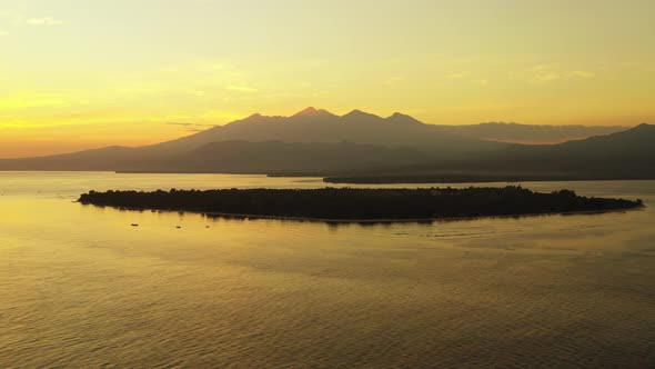 Peaceful gold sunset over a quiet scenery with low-lying tropical island surrounded by calm sea refl