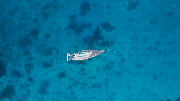 Yacht swaying and bobbing in the ocean revealing reef in the clear blue waters. High view looking do