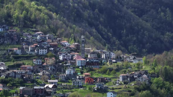 Remote Villadossola town with clock tower in green Italian Alp hillside; drone