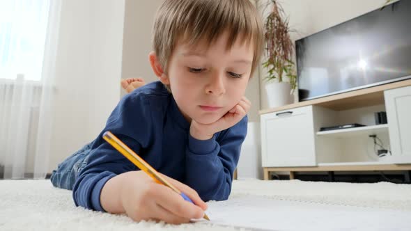 Little Boy Doing Homework in Copybook While Lying on Carpet in Living Room