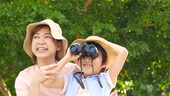 Asian Mother And Her Son Using Binocular And Pointing On Summer Day