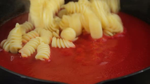 Putting pasta penne in pan with tomato sauce in pan, close up