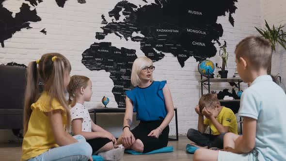 Group of Small Pupils From Five Children Sitting on Floor and Listening to Teacher