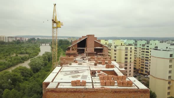 Aerial view of unfinished brick apartment building with wooden roof structure under construction.