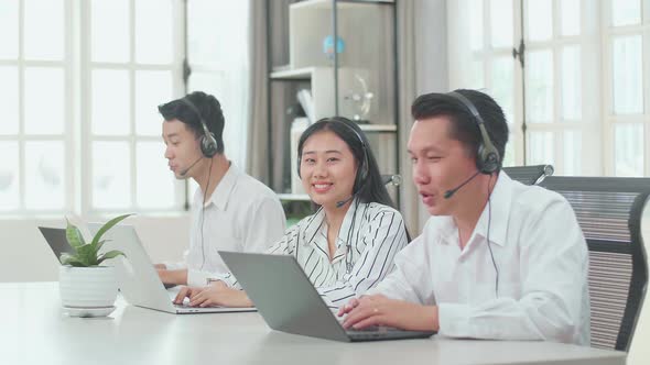 A Woman Of Three Asian Call Centre Agents Smile To Camera Then Thumbs Up While Colleagues Working