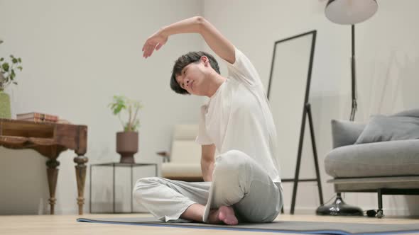 Young Asian Man Doing Stretches on Yoga Mat at Home