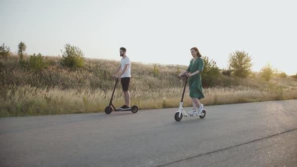 The Couple in Love Riding on Electric Scooters with Joy on the Asphalt Road