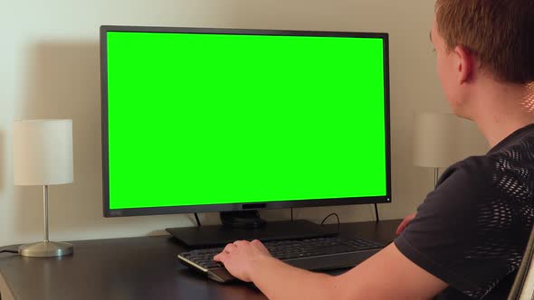 A Man Sits at a Table and Looks at a Green Computer Screen