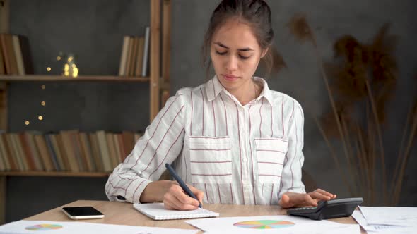 Focused Young Woman Looking Through Paper Documents with Charts Accounting Alone at Home Office