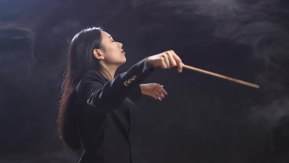 Asian Conductor Woman Holding A Baton And Showing Gesture Quickly In The Black Studio With Fog