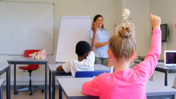 Schoolkids raising hand while sitting at desk in elementary school 4k