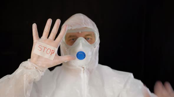 Virologist in White Protective Suit, Mask and Gloves Showing Stop Virus on Black Background