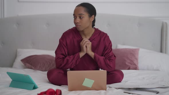 Portrait of Thoughtful African American Young Woman Sitting on Bed Examining Business Graph