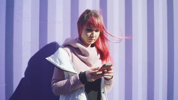 Independent Young Woman with Pink Hair Uses Smartphone on Purple Containers Background