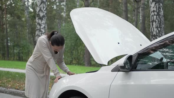 Young Woman Looks Under the Hood of Broken Car