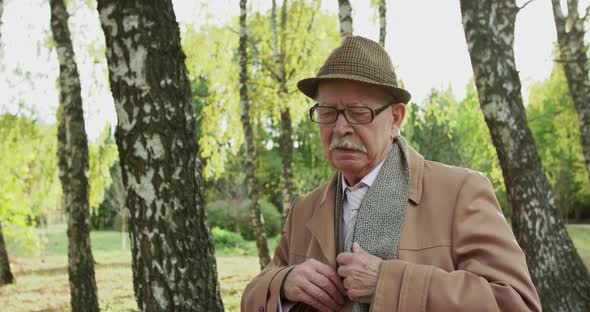 Elegant Senior Man Pulls Out His Phone Dials and Calls in a Sunny Park