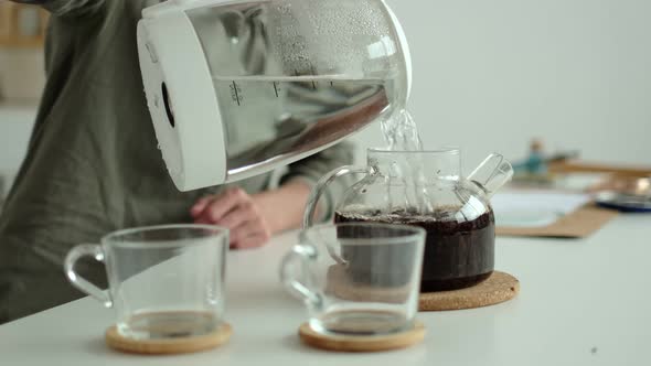 Woman Pours Hot Water From an Electric Kettle Into a Teapot with Loose Tea