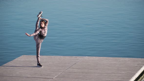 young athletic girl with a great stretch is the splits on pier against blue lake