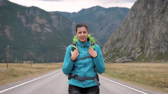Young Hipster Woman With Backpack Walks Along Road In Mountains