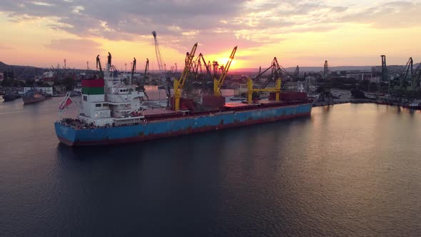 Aerial View of Cargo Ship Bulk Carrier is Loaded with Grain of Wheat in Port at Sunset