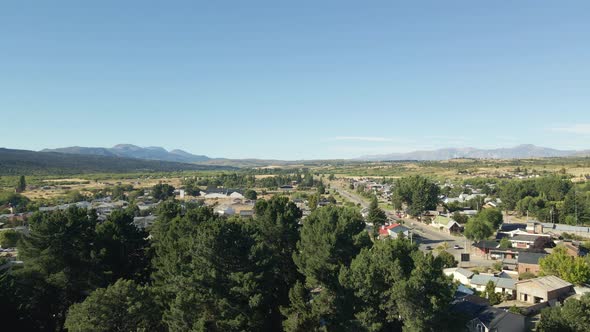 Aerial pan left of Trevelin town houses surrounded by forest and Andean mountains, Patagonia Argenti