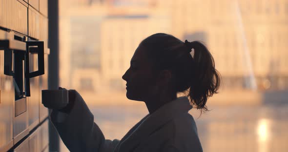 Young Woman in Bathrobe Making Coffee with Coffee Machine in Kitchen at Home