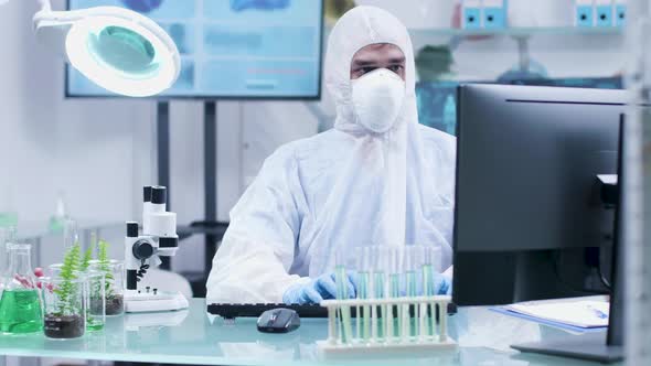 Biotechnologist in White Coverall and Mask Working on Computer