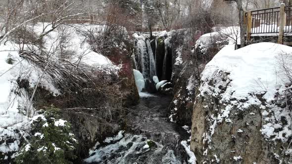 Flying back away from waterfall with snow in winter in 4K