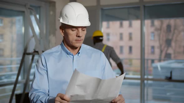 Engineer Wearing Safety Helmet Looking at Blueprint on Construction Site