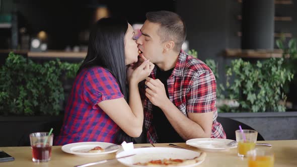 man and a woman are eating one slice of pizza from two sides at the table in the restaurant