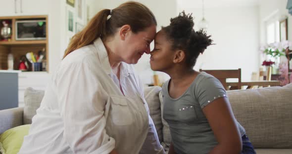 Happy caucasian woman and her african american daughter smiling in living room