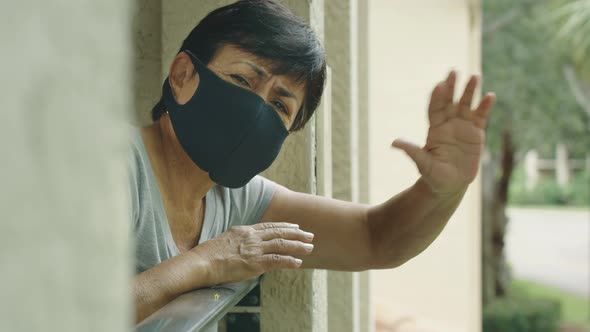 Elderly Woman Wearing Protective Face Mask Waving From Her Balcony