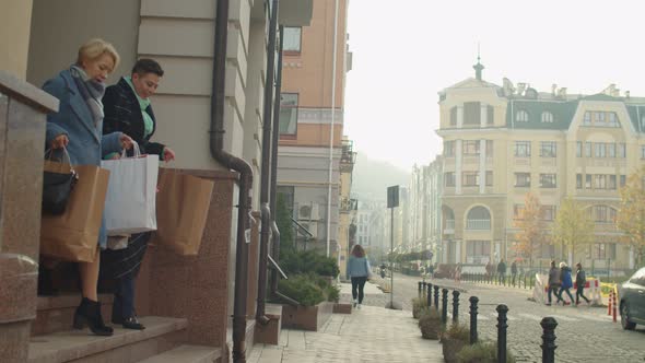 Two Female Buyers with Many Paper Bags Walking Downstairs Outdoors