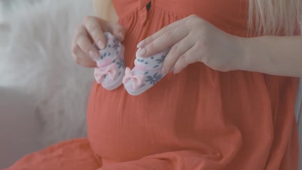 Close-up of Young Caucasian Female Hands Holding Baby Booties and Imitating Stepping on Pregnant