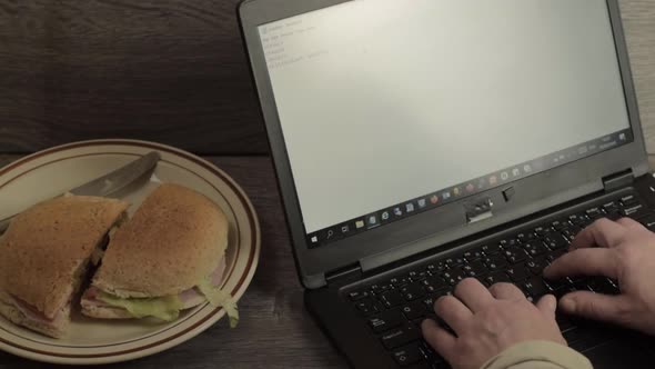 Busy person typing on a laptop while grabbing a sandwich