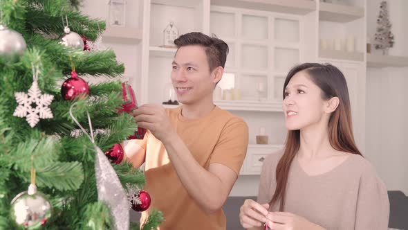 Asian couple feeling happy decorating christmas tree in their living room at home.