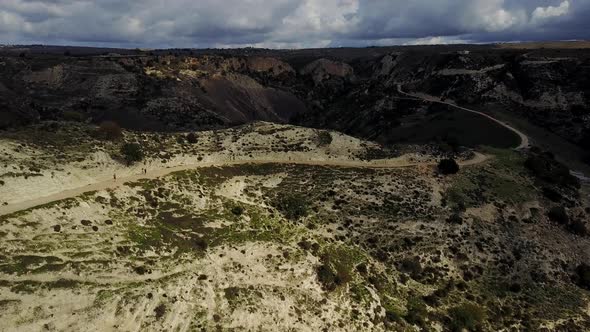 Wide aerial view of a group of runners who are jogging up a path on the side of the mountain in Akam