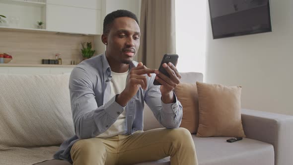 Young Adult 20s African American Man Browsing on His Smartphone in His Apartment