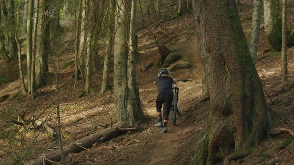 Mountain biker pushes his bike up a steep hill in the forest