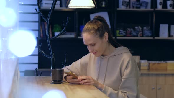 A young woman using smartphone in a evening cafe, drink coffee.