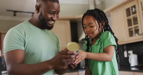 Happy african american father and daughter reading label on can in kitchen